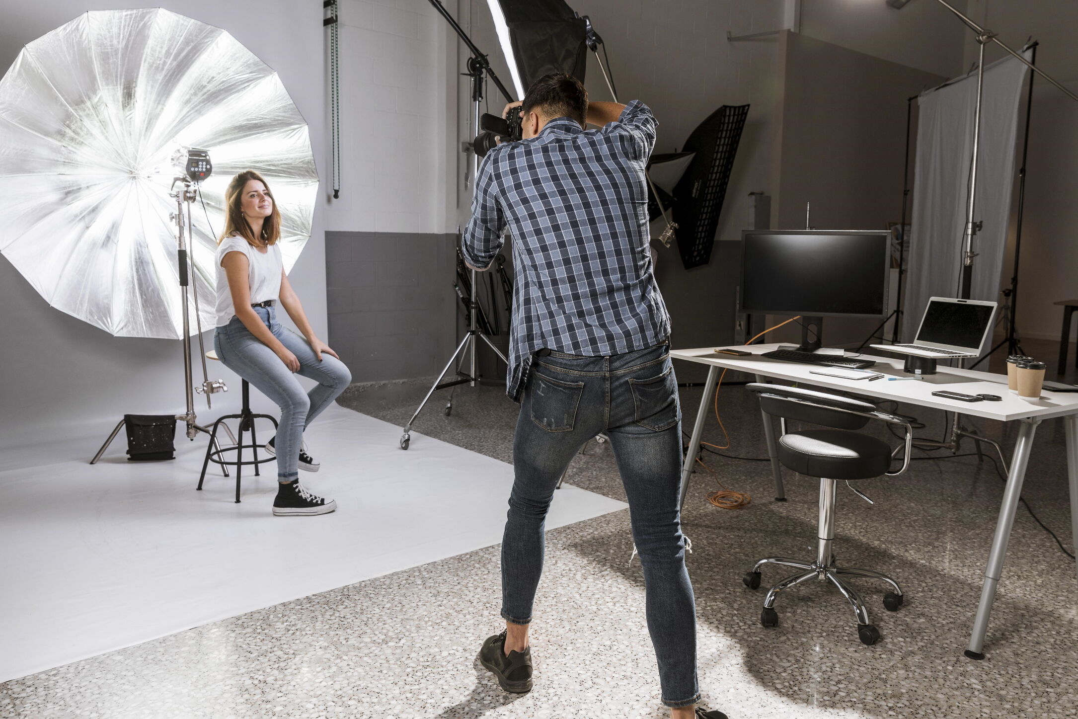 Junger Fotograf der stehend von einem sitzenden, weiblichen Model Schnappschüsse nimmt.